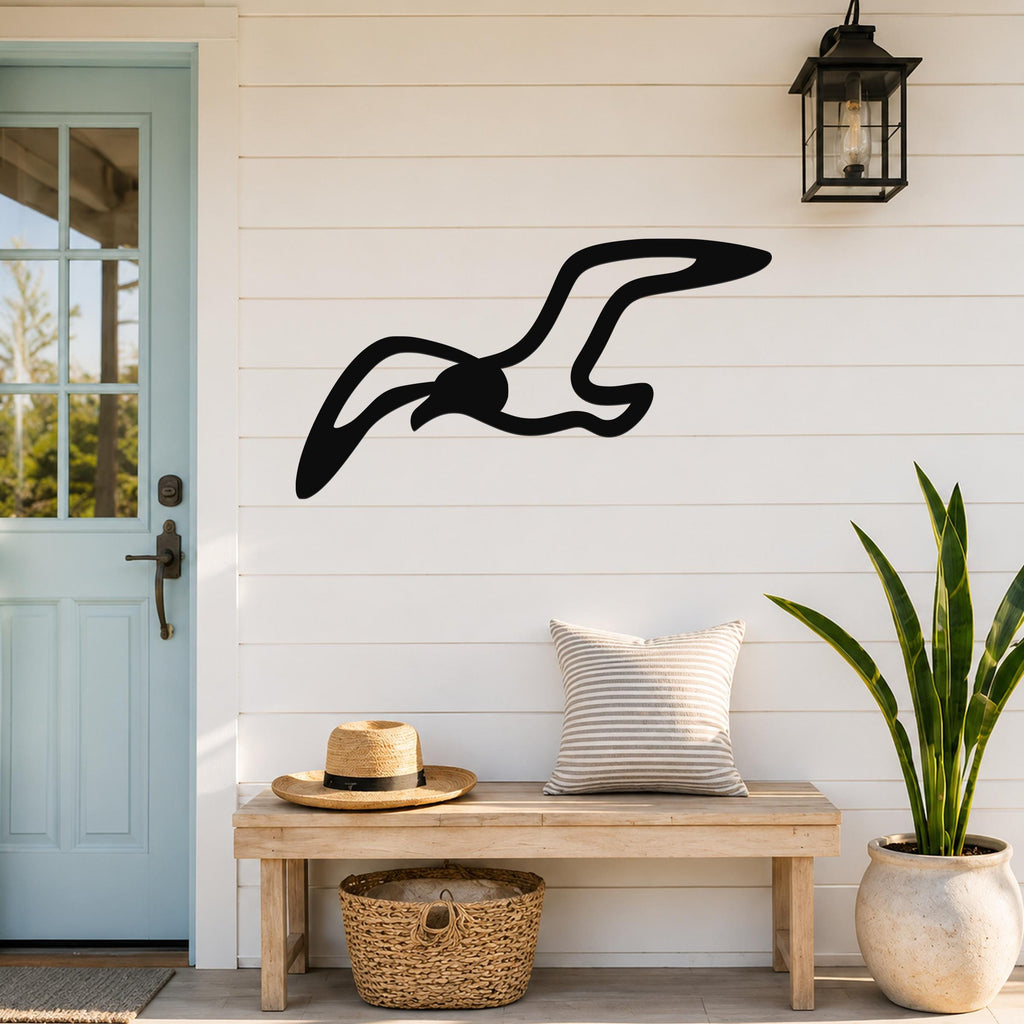 Black metal seagull wall art with flowing wing cutouts, mounted on a white shiplap wall above a wooden bench in a coastal entryway.