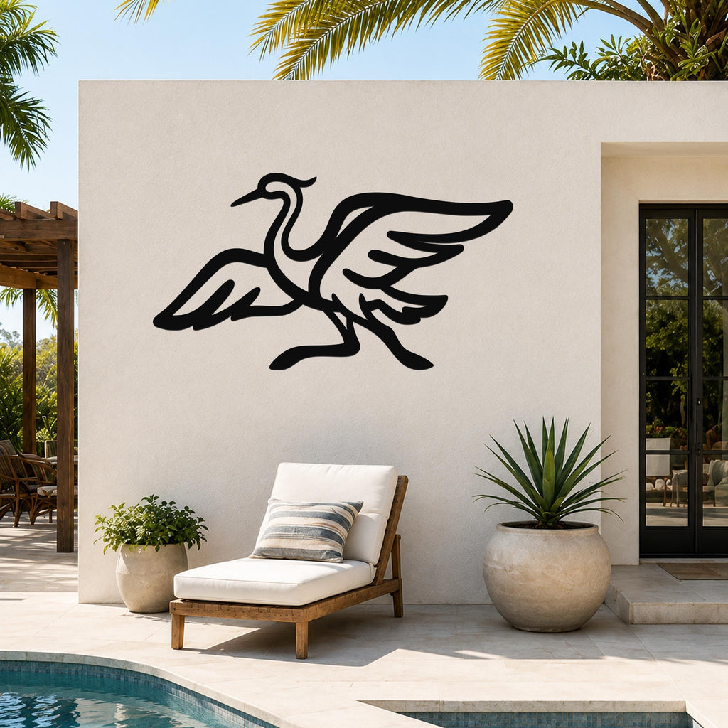 Black metal crane wall art silhouette with extended wings and long legs, mounted on an outdoor patio wall above a lounge chair.