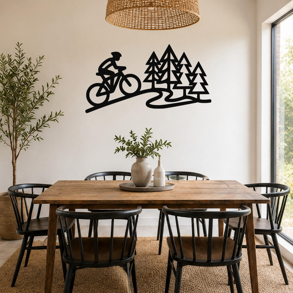 Black metal wall art featuring a cyclist silhouette and pine trees, mounted on a dining room wall above a wooden table.