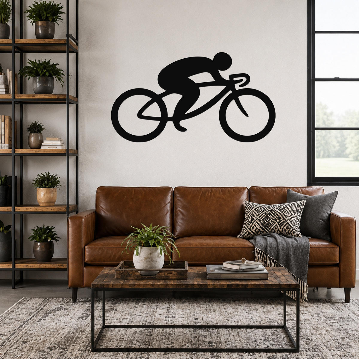 Black metal cycling wall art silhouette of a cyclist on a road bike, mounted above a brown leather sofa in a living room.