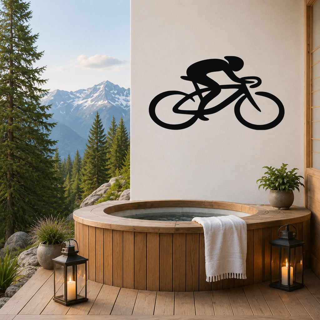 Black metal wall art silhouette of a cyclist on a bike, mounted on a white wall above a wooden hot tub on a mountain-view deck.