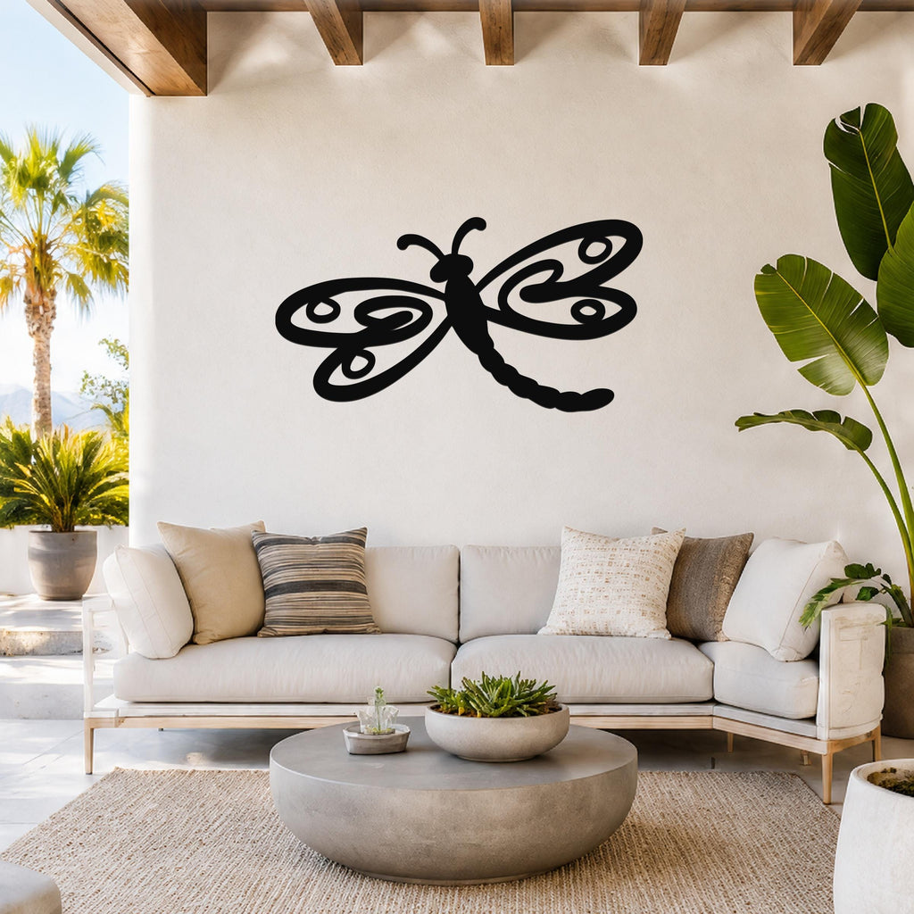 Black metal dragonfly wall art with intricate wing cutouts, mounted on a white wall above a light-colored sofa in a bright living room.