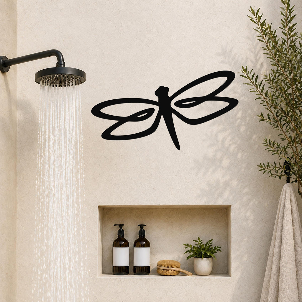 Black metal dragonfly wall art with flowing wing cutouts, mounted on a bathroom wall above a built-in shelf.