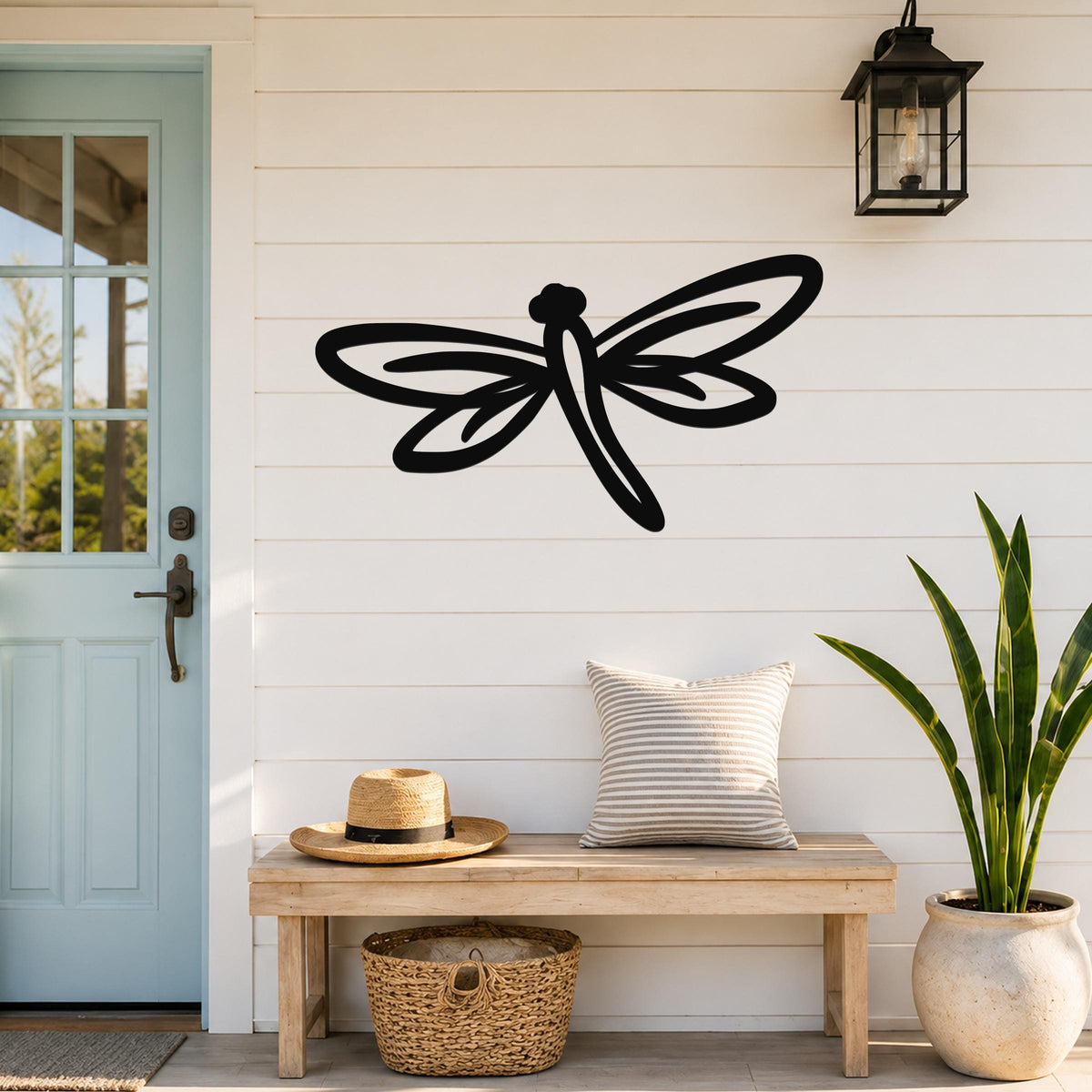 Black metal dragonfly wall art with cutout wings and body, mounted on a white shiplap wall above a wooden bench in a porch entryway.