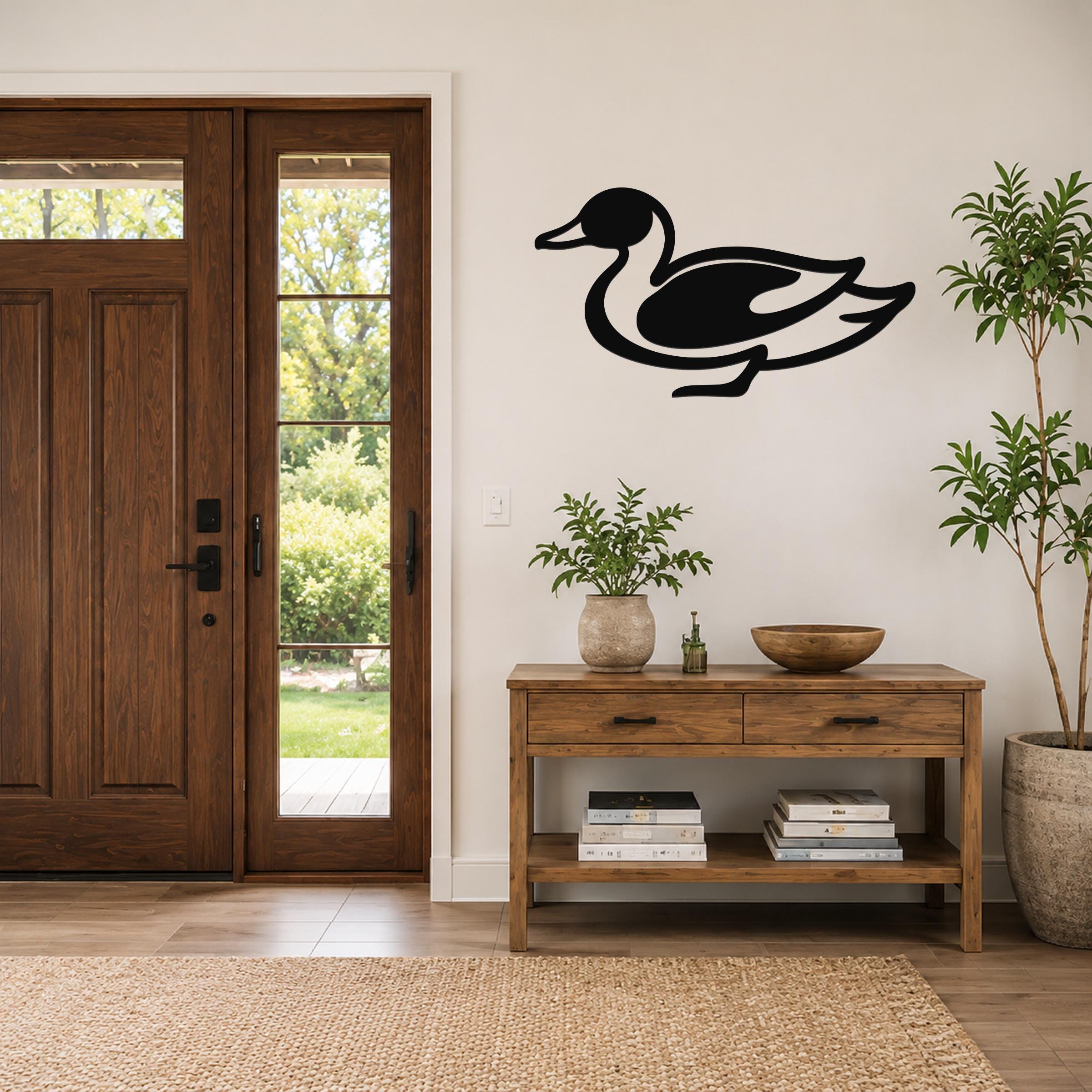 Black metal duck wall sculpture with a cutout silhouette, mounted on a white wall above a wooden console table in a modern entryway.