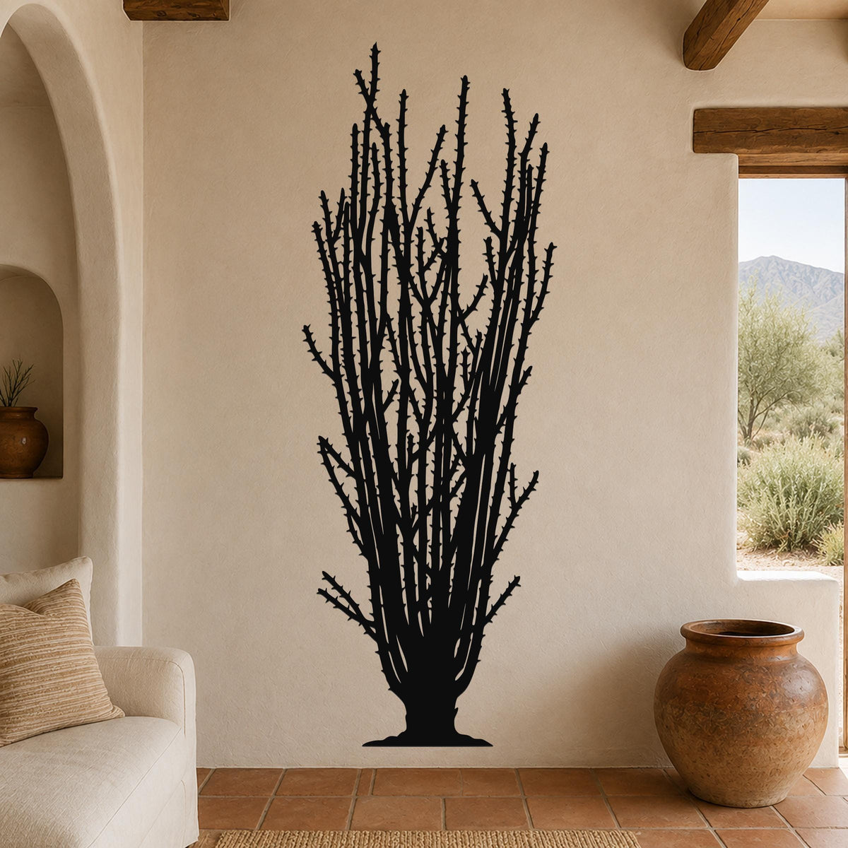 Black metal wall art silhouette of a tall ocotillo cactus with spiny branches, mounted on a beige living room wall above a sofa.