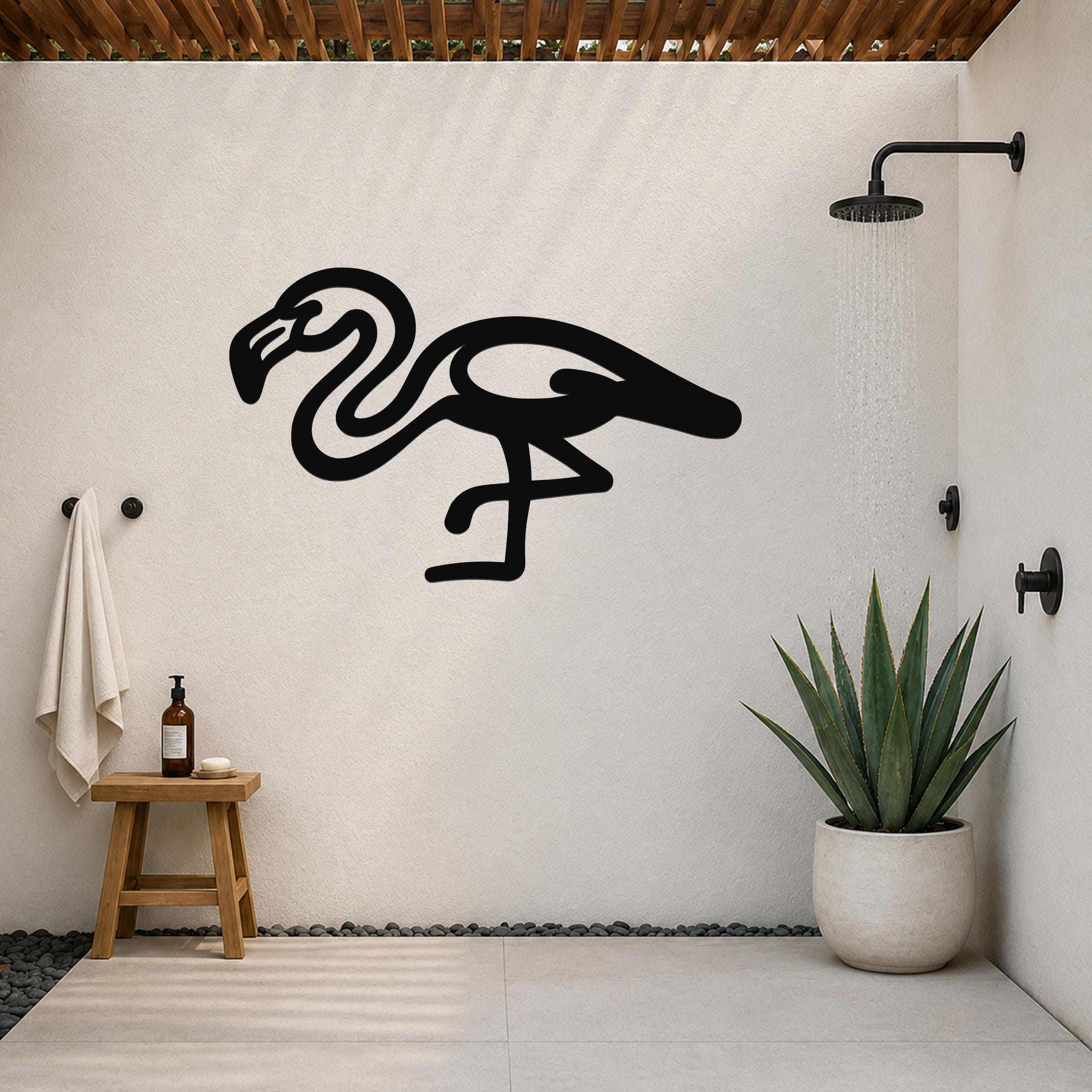Black metal flamingo wall art with a minimalist silhouette design, mounted on a white outdoor shower wall above a small wooden stool and a potted succulent.