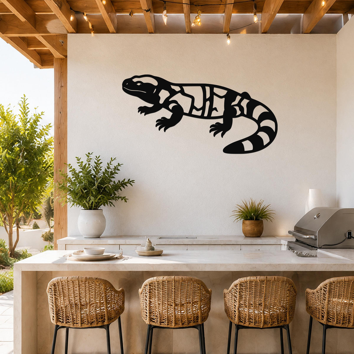 Black metal Gila monster wall art with internal cutout patterns, mounted on a white wall above a kitchen counter in an outdoor patio setting.