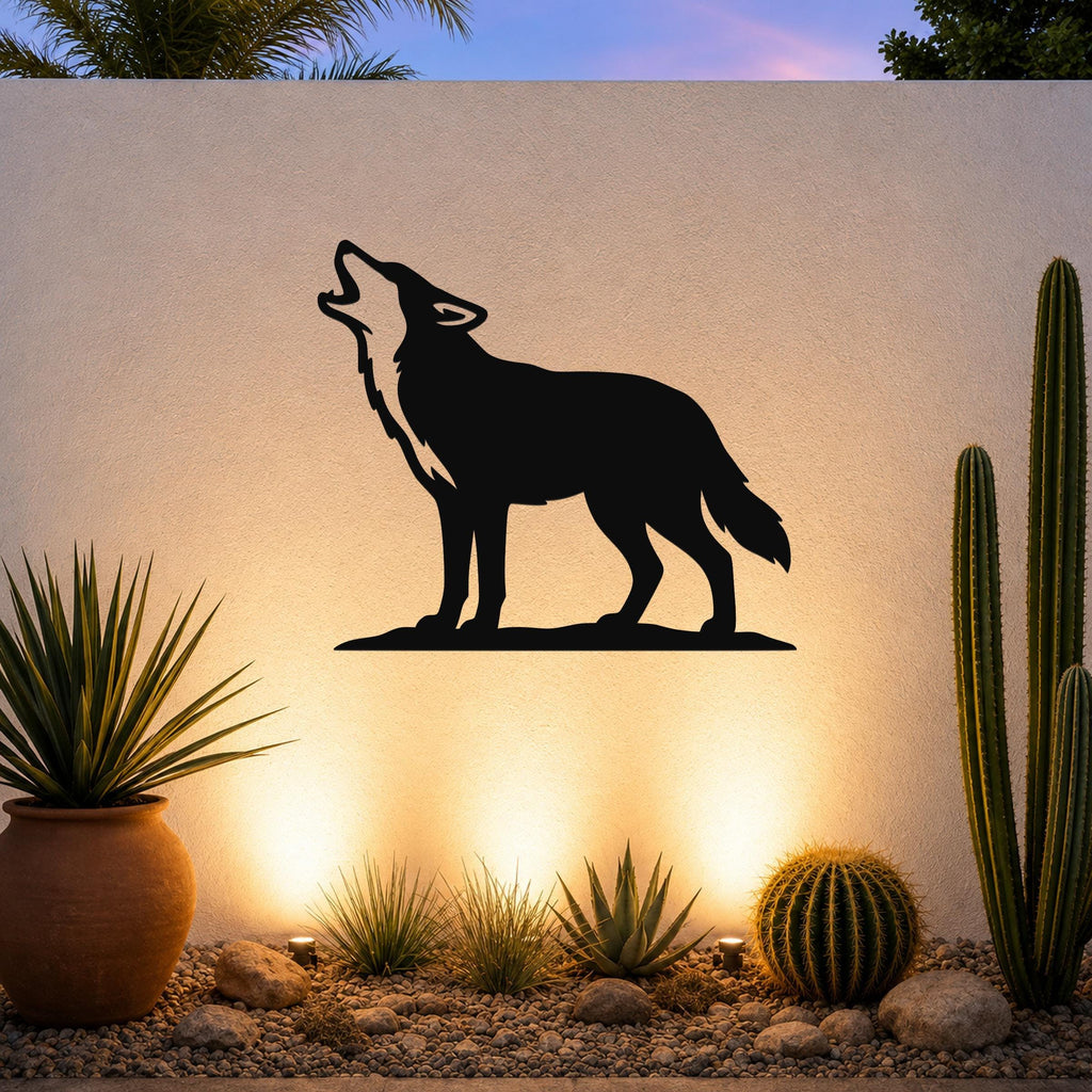 Black metal coyote howling wall art silhouette mounted on a light-colored outdoor wall above a desert garden with cacti and warm uplighting.