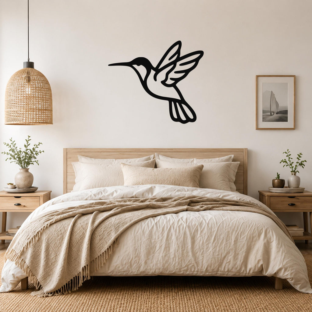 Black metal hummingbird wall art in silhouette style, mounted above a bed in a neutral bedroom.