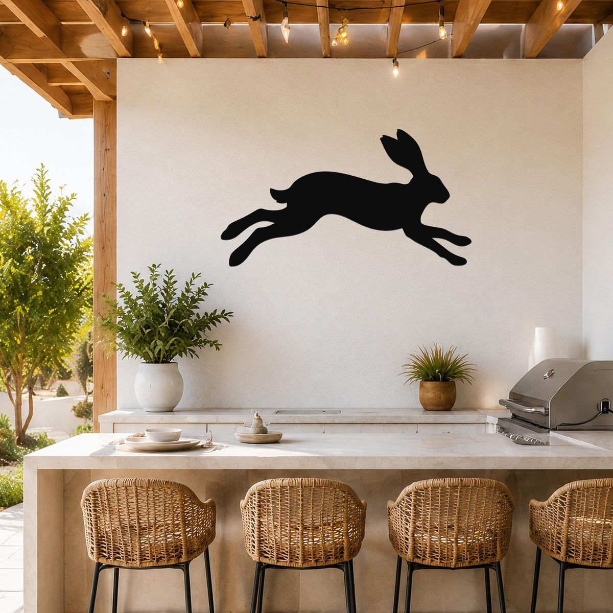 Black metal jackrabbit wall art silhouette mounted on a white outdoor wall above a kitchen counter with wicker bar stools.