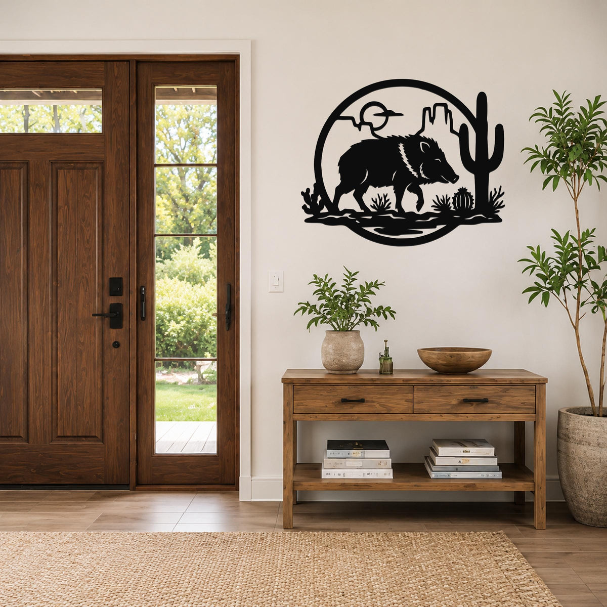 Black metal wall art featuring a javelina silhouette with cactus and desert landscape cutouts, mounted on a wall above a wooden console table in a entryway.