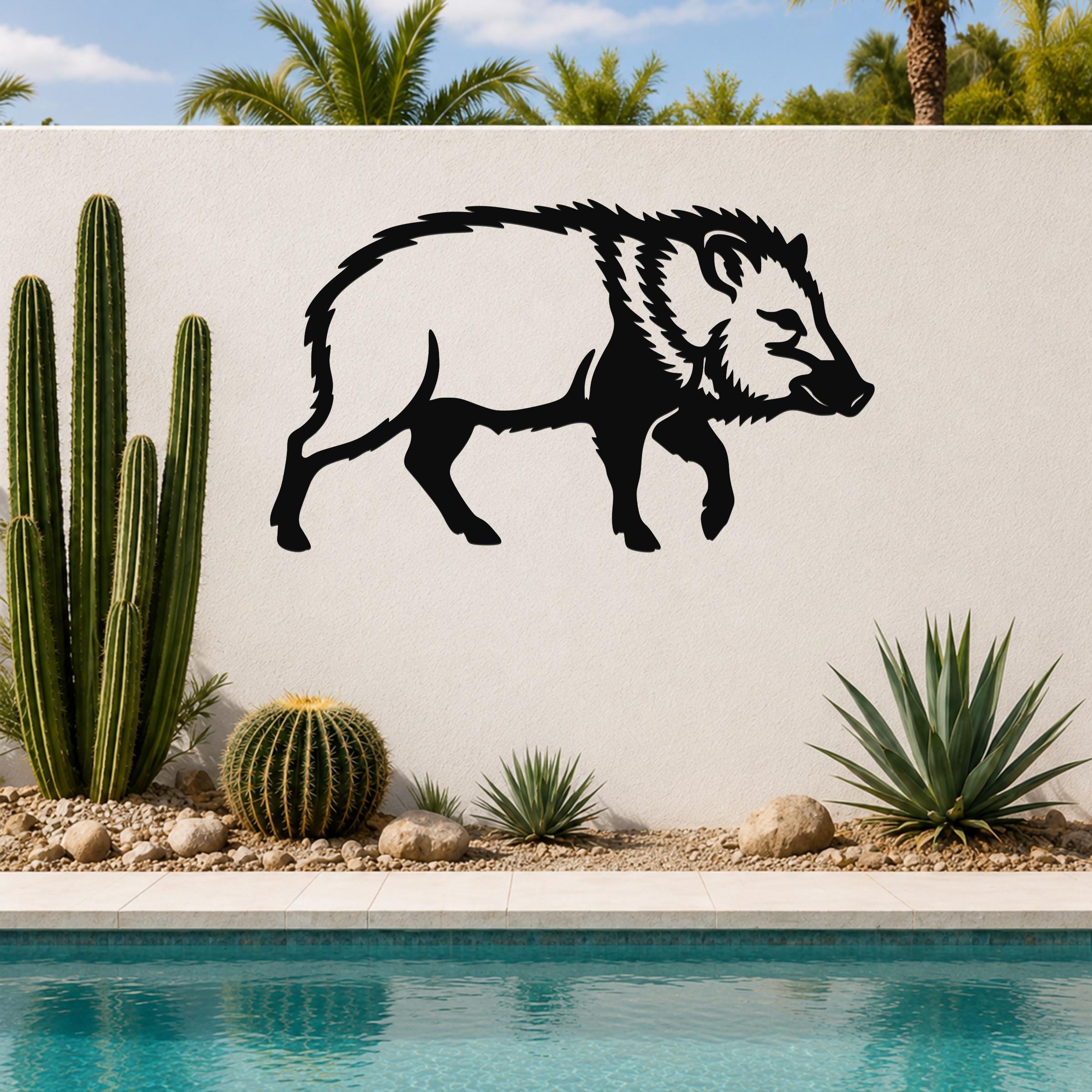 Black metal javelina wall art silhouette mounted on a white outdoor wall above a pool, with cacti and desert plants in the foreground.