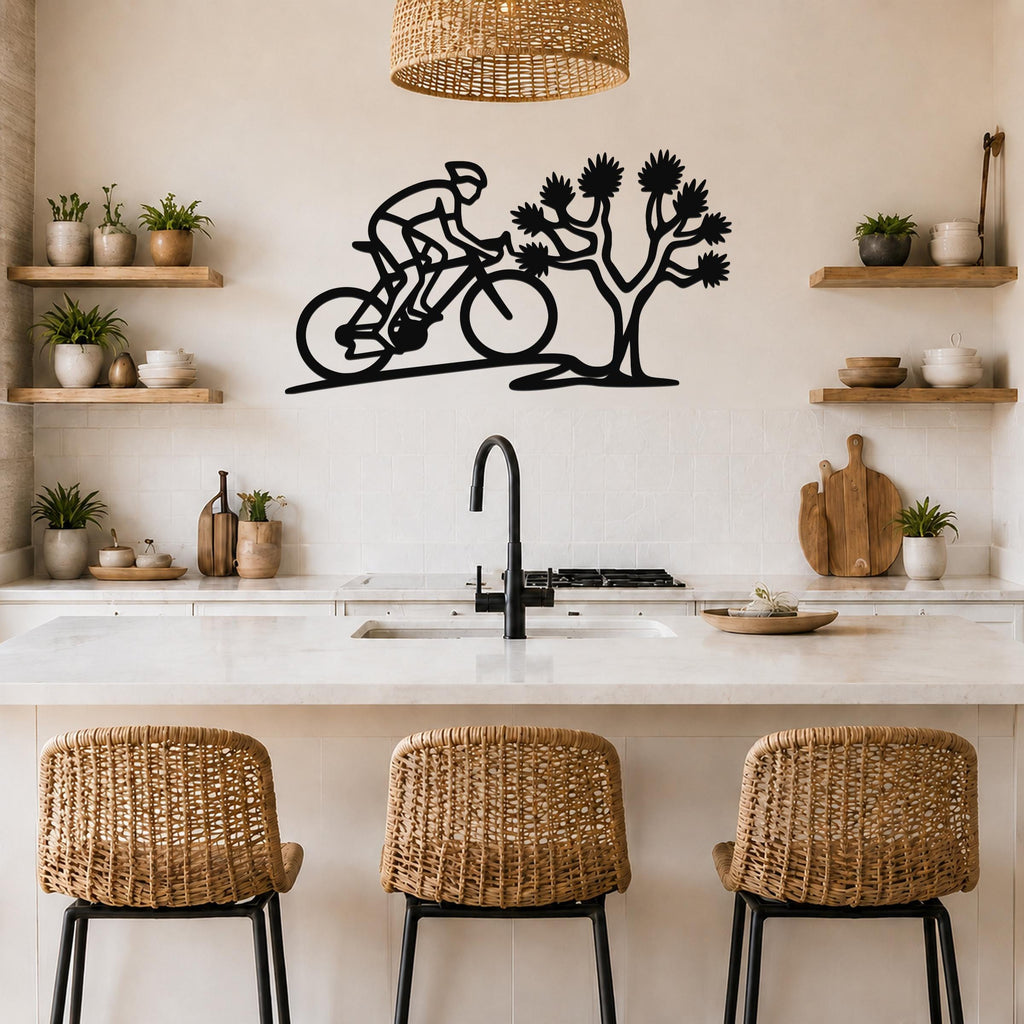 Black metal wall art cutout of a cyclist and a Joshua tree, mounted above a kitchen counter with wicker bar stools.