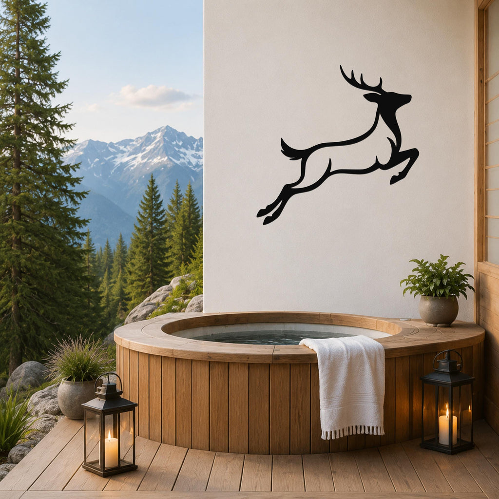 Black metal jumping deer wall art silhouette mounted on a white wall above a wooden hot tub on a mountain-view deck.