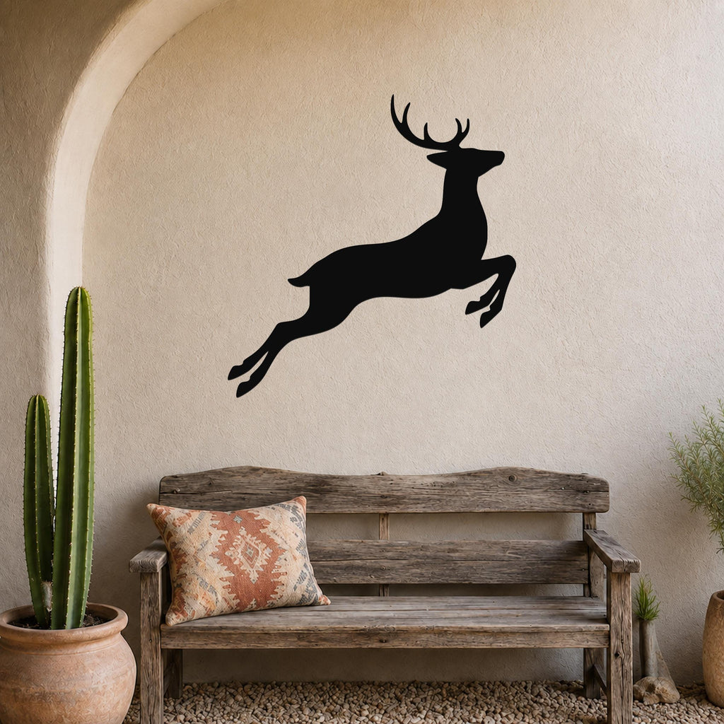 Black metal deer wall art in a jumping silhouette, mounted on a textured beige wall above a rustic wooden bench in a patio setting.