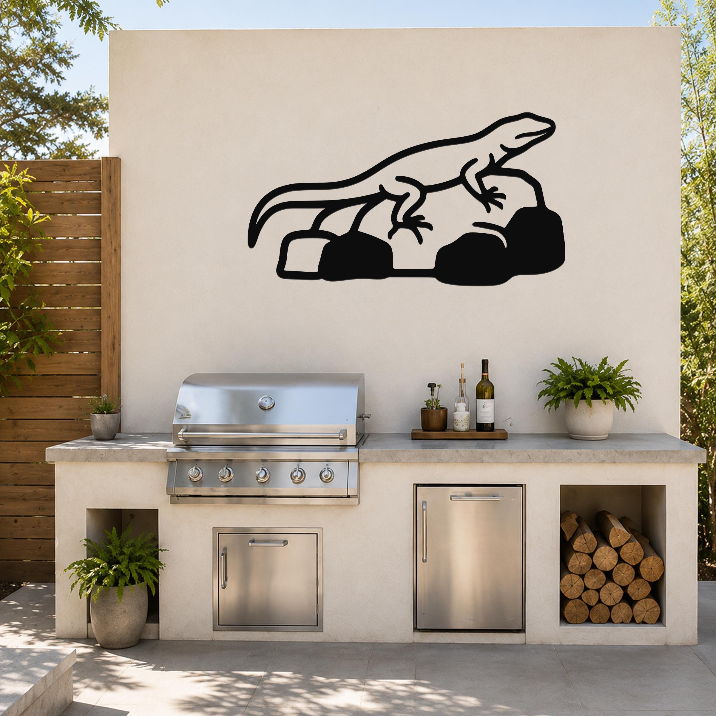 Black metal lizard wall art silhouette mounted on an outdoor kitchen wall above a stainless steel grill and counter.