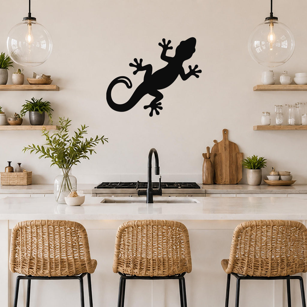 Black metal gecko wall art silhouette mounted on a kitchen wall above a counter, with visible cutout details of the lizard's limbs and tail.