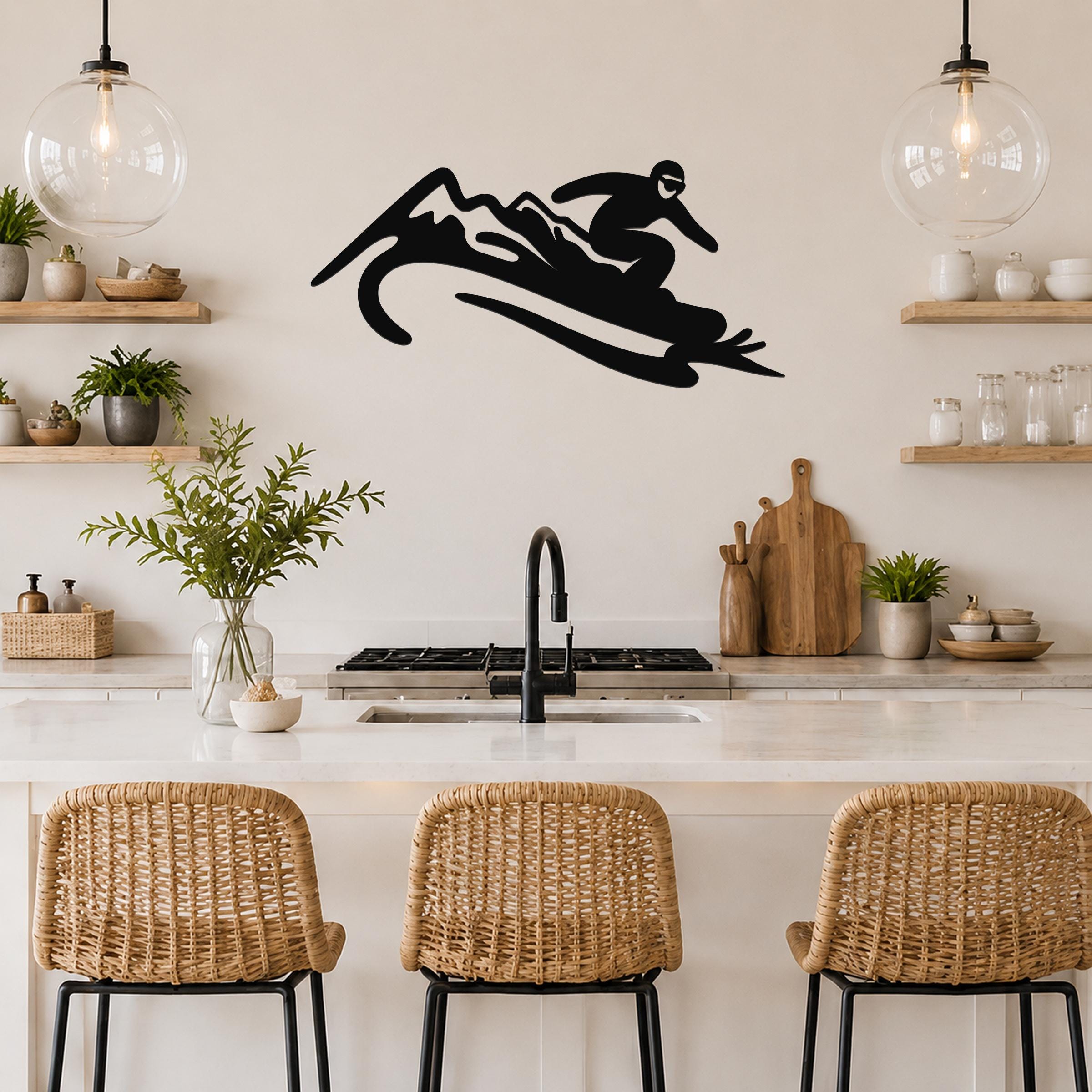 Black metal wall art silhouette of a snowboarder in motion, mounted above a kitchen counter with wicker bar stools.