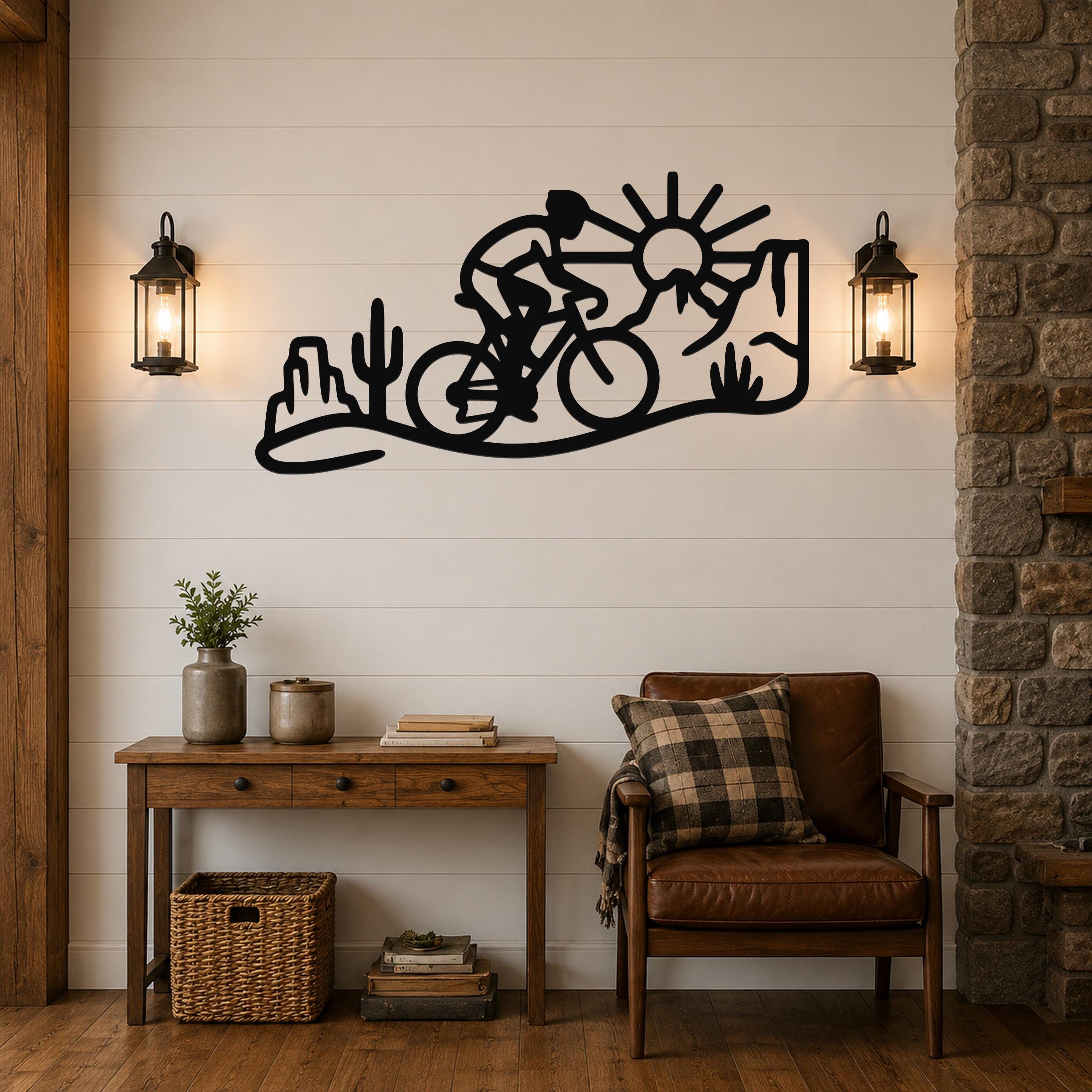 Black metal wall art silhouette of a cyclist in a desert scene with cacti and sun, mounted on a shiplap wall above a wooden console table in a living room.