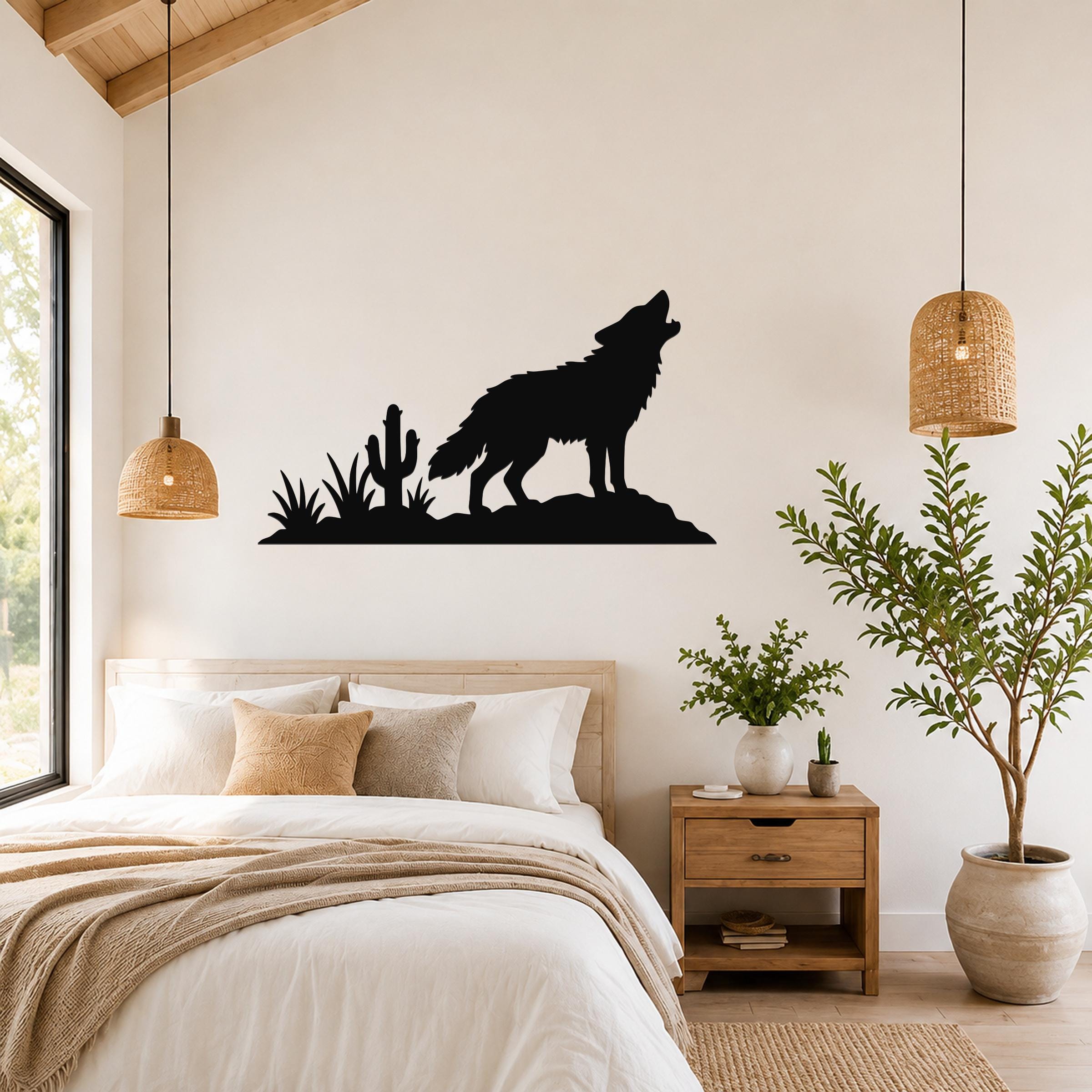 Black metal wall art silhouette of a coyote howling on a rock with cactus and desert plants, mounted above a bed in a bedroom.