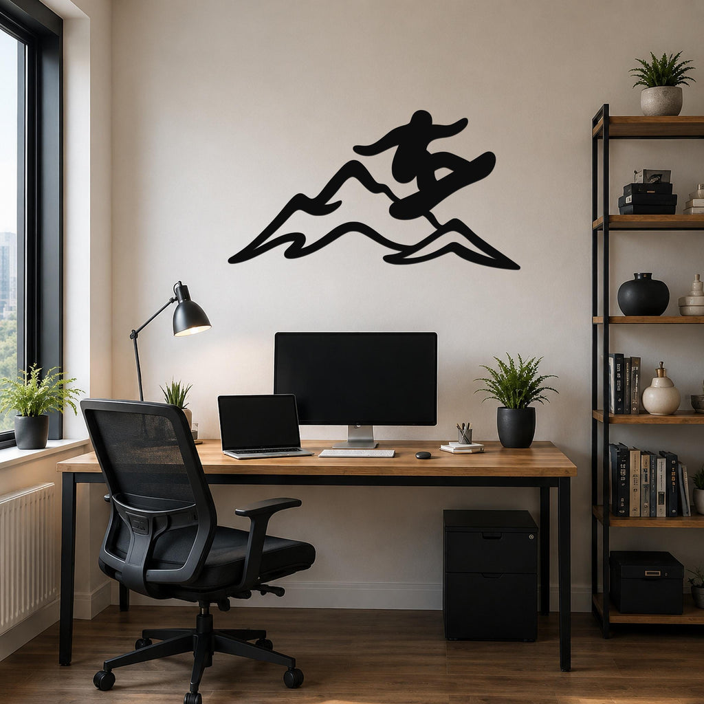 Black metal wall art silhouette of a snowboarder in motion over mountain peaks, mounted above a wooden desk in a home office.