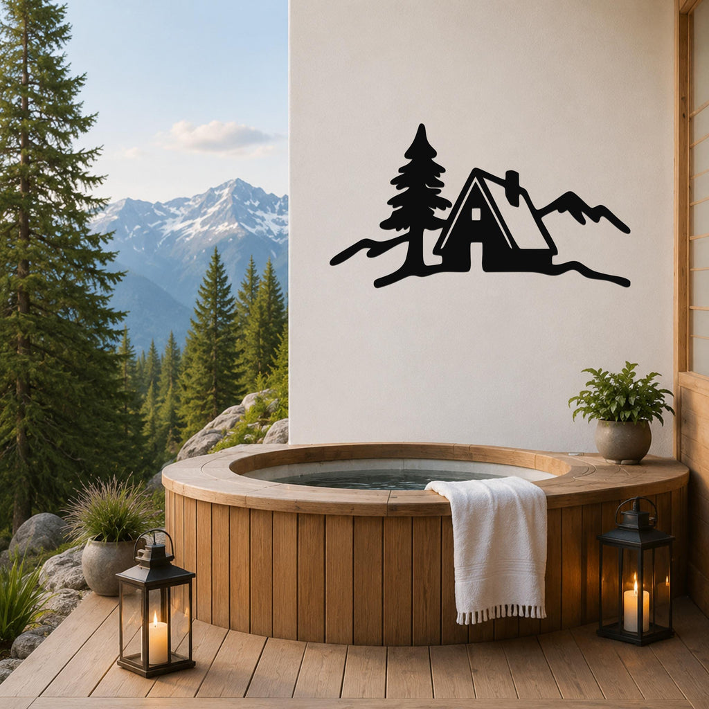 Black metal wall art silhouette of a cabin, tree, and mountains, mounted on a white wall above a wooden hot tub on a deck with a mountain view.