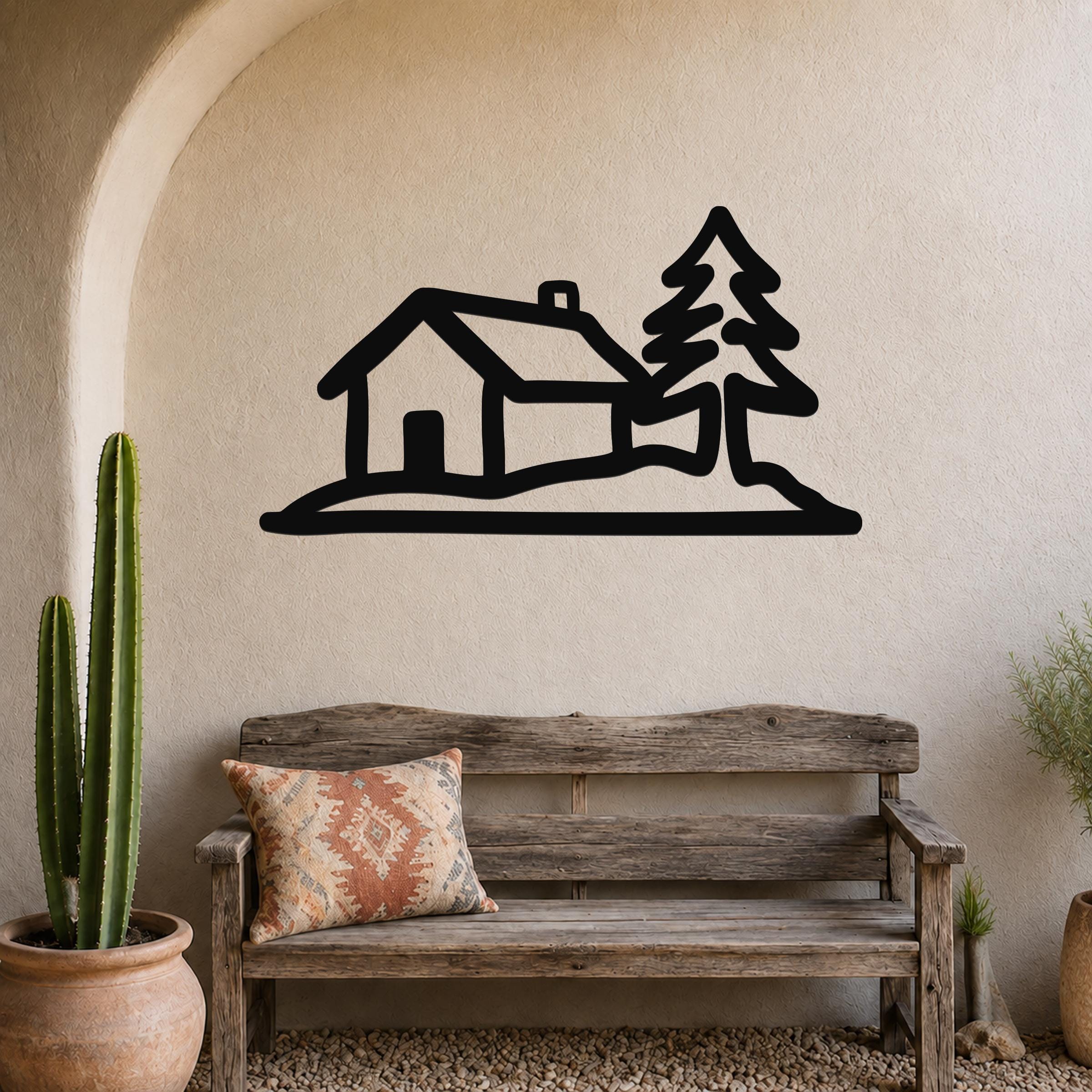 Black metal wall art silhouette of a cabin and pine tree, mounted on a textured wall above a wooden bench in a rustic entryway.