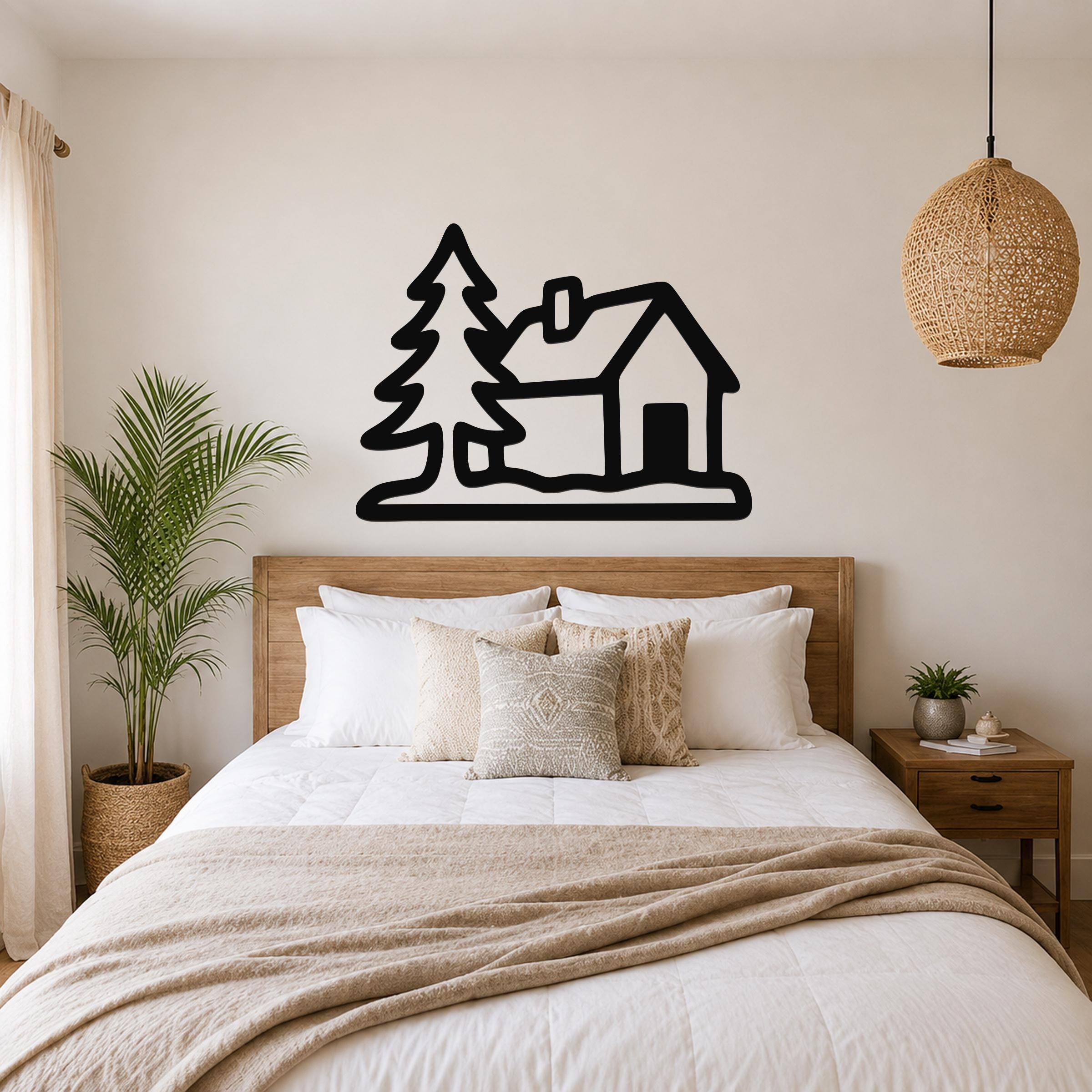 Black metal wall art silhouette of a cabin and pine tree, mounted above a wooden bed in a bedroom.