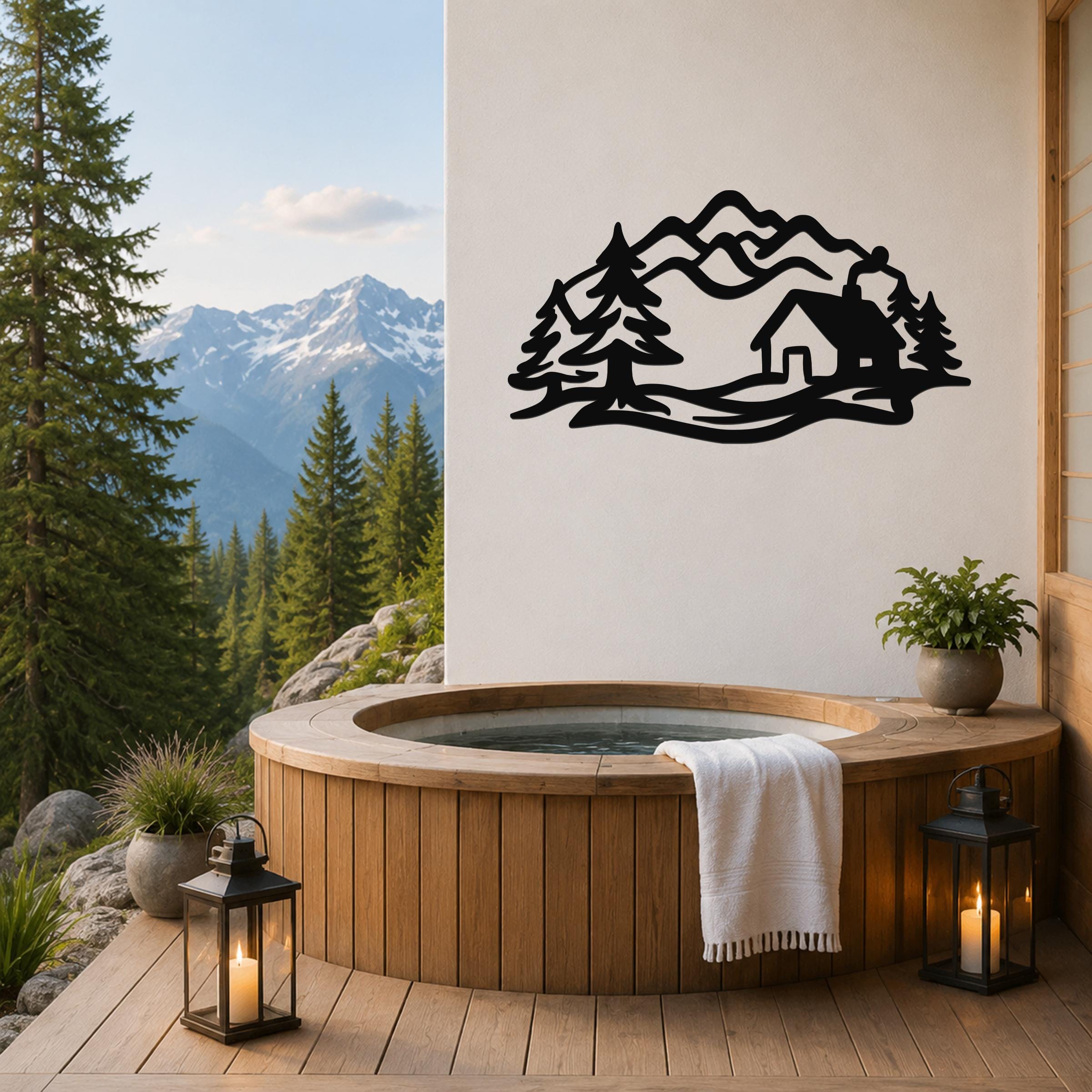 Black metal wall art silhouette of a mountain cabin surrounded by trees, mounted on a white wall above a wooden hot tub on a deck with a mountain view.