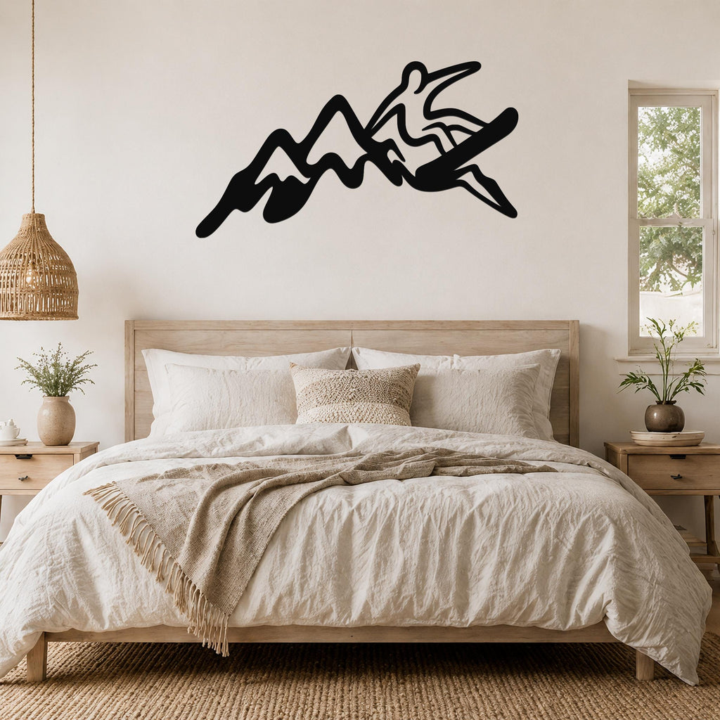 Black metal wall art silhouette of a snowboarder in motion over mountain peaks, mounted above a bed in a bedroom.