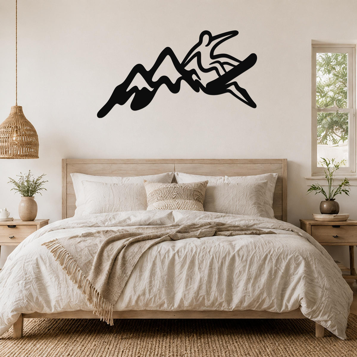 Black metal wall art silhouette of a snowboarder in motion over mountain peaks, mounted above a bed in a bedroom.