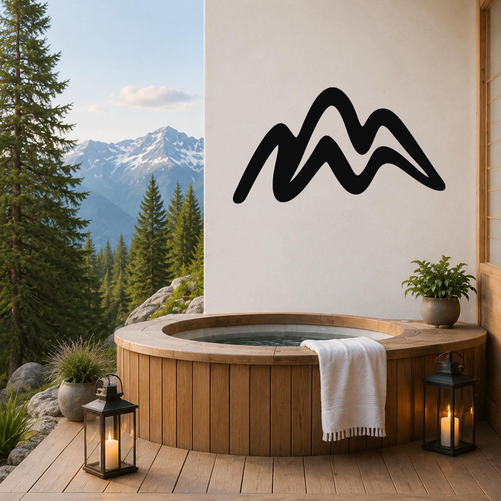 Black metal mountain silhouette wall art mounted on a white wall above a wooden hot tub on a deck with a mountain view.