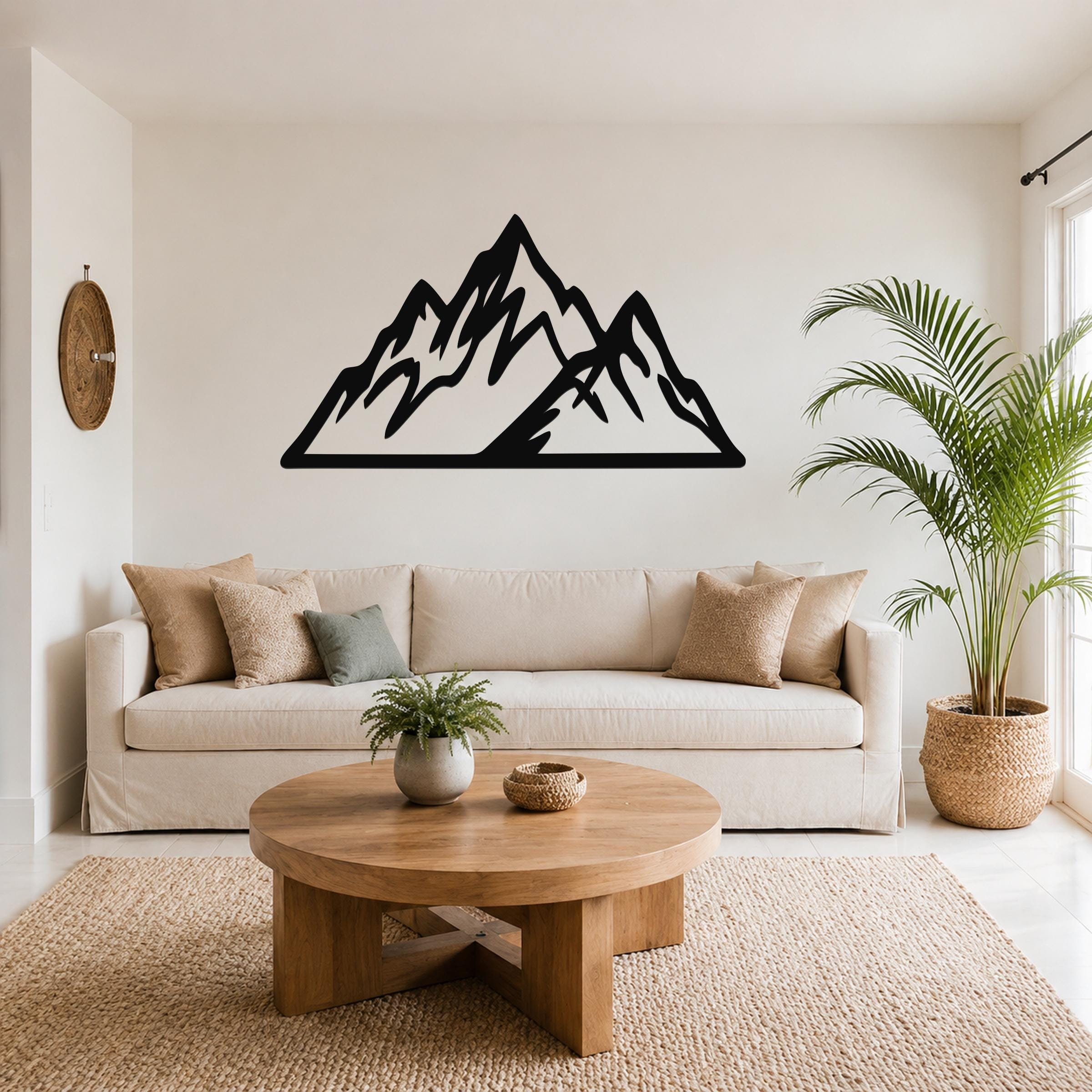 Black metal mountain wall art with jagged peak cutouts, mounted above a beige sofa in a living room.