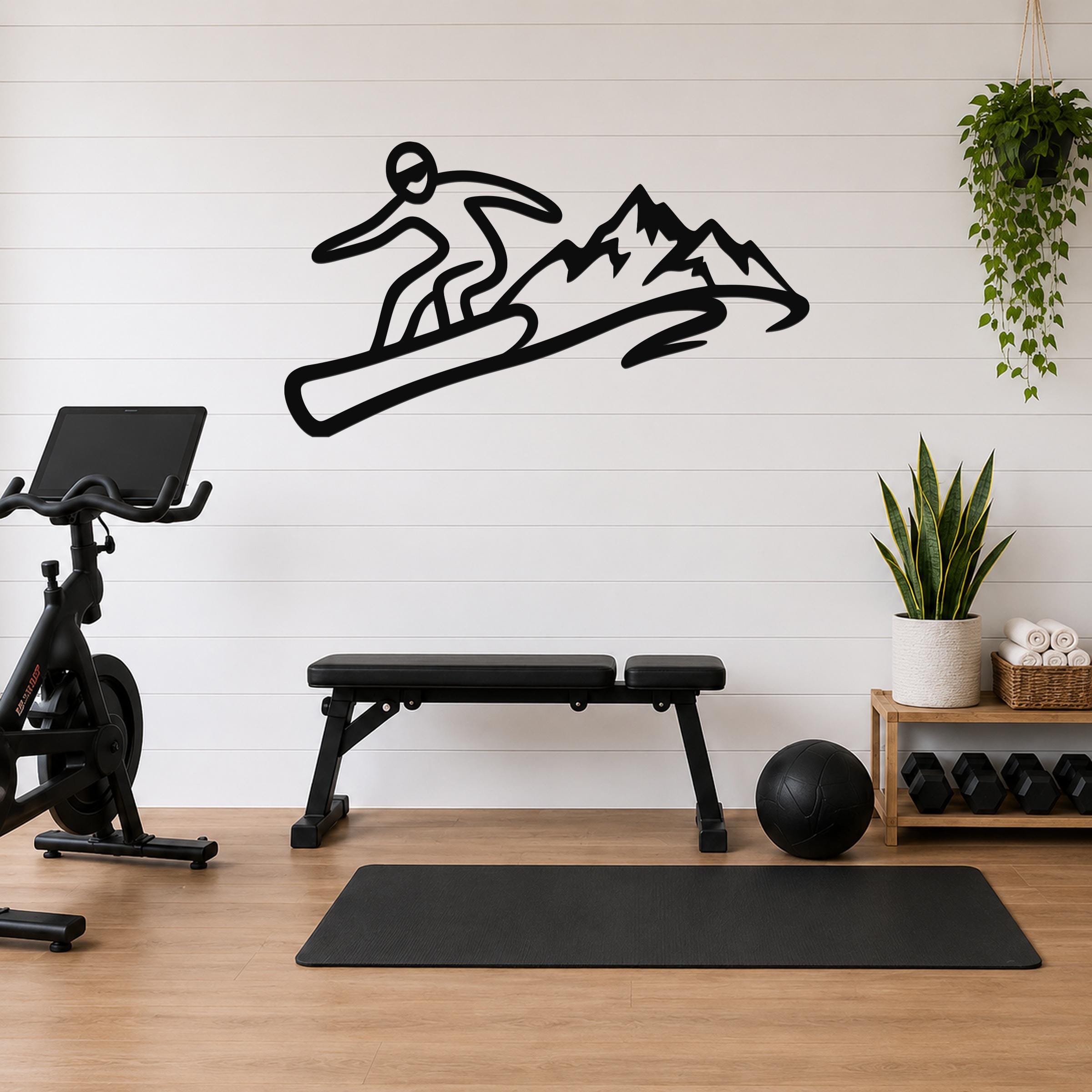 Black metal wall art featuring a snowboarder silhouette in dynamic motion above mountain peaks, mounted on a white shiplap wall above a workout bench in a home gym.