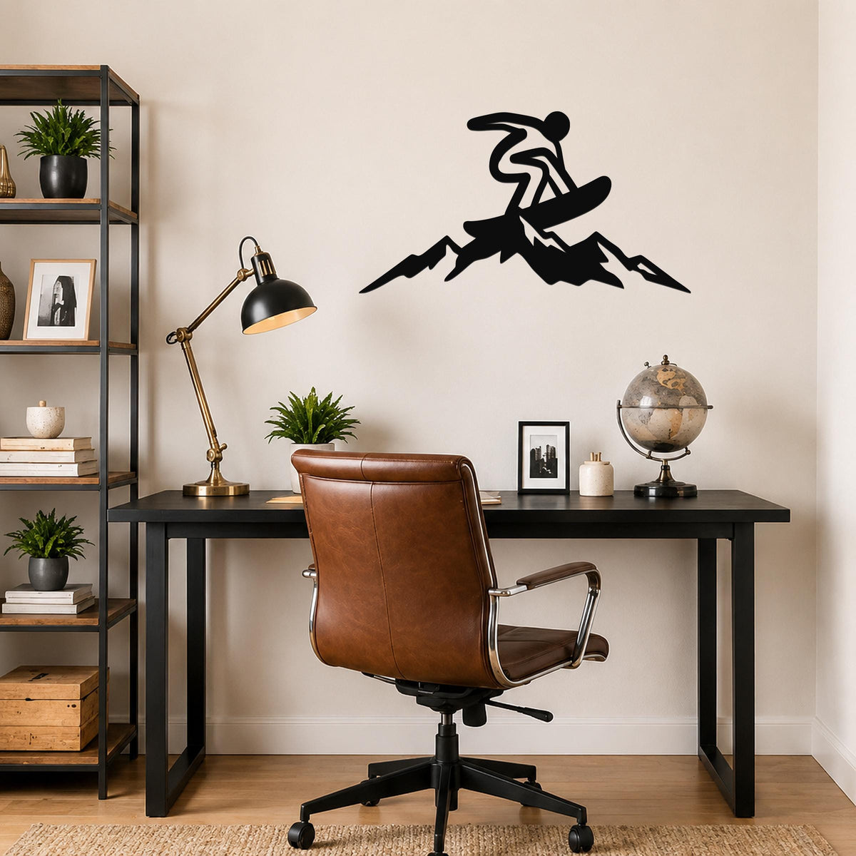 Black metal wall art silhouette of a snowboarder in motion above a mountain peak, mounted on a wall above a black desk in a home office.