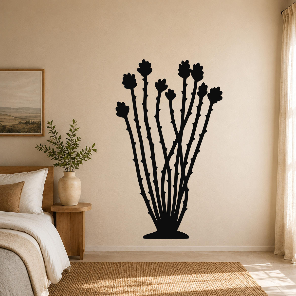 Black metal ocotillo wall art with spiny stems and flower cutouts, mounted on a beige bedroom wall above a woven rug.