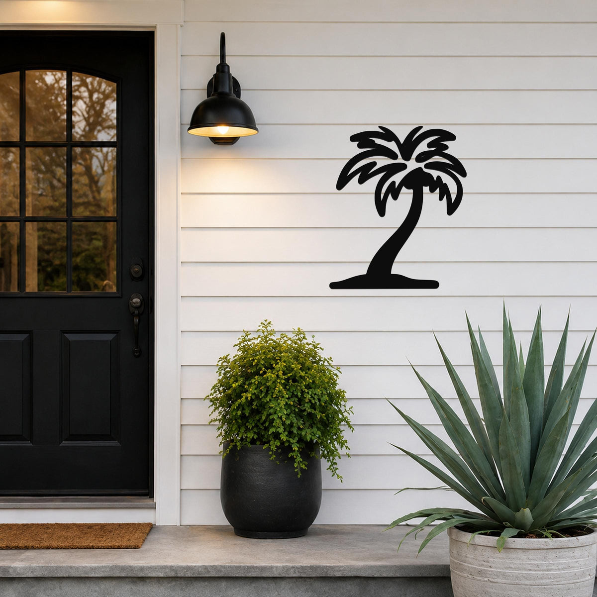 Black metal palm tree wall art silhouette mounted on a white horizontal siding wall beside a black front door and outdoor light.