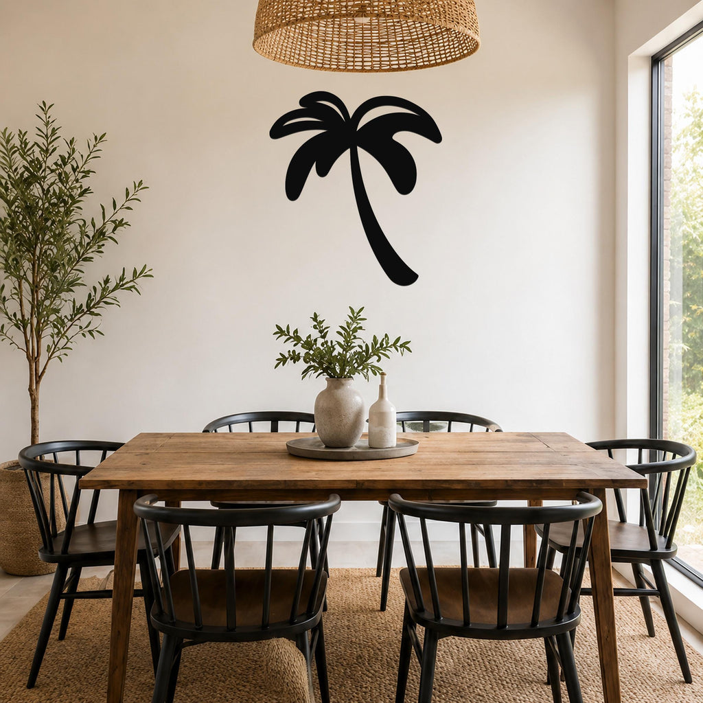 Black metal palm tree wall art silhouette mounted on a white wall above a wooden dining table in a bright, coastal-style dining room.
