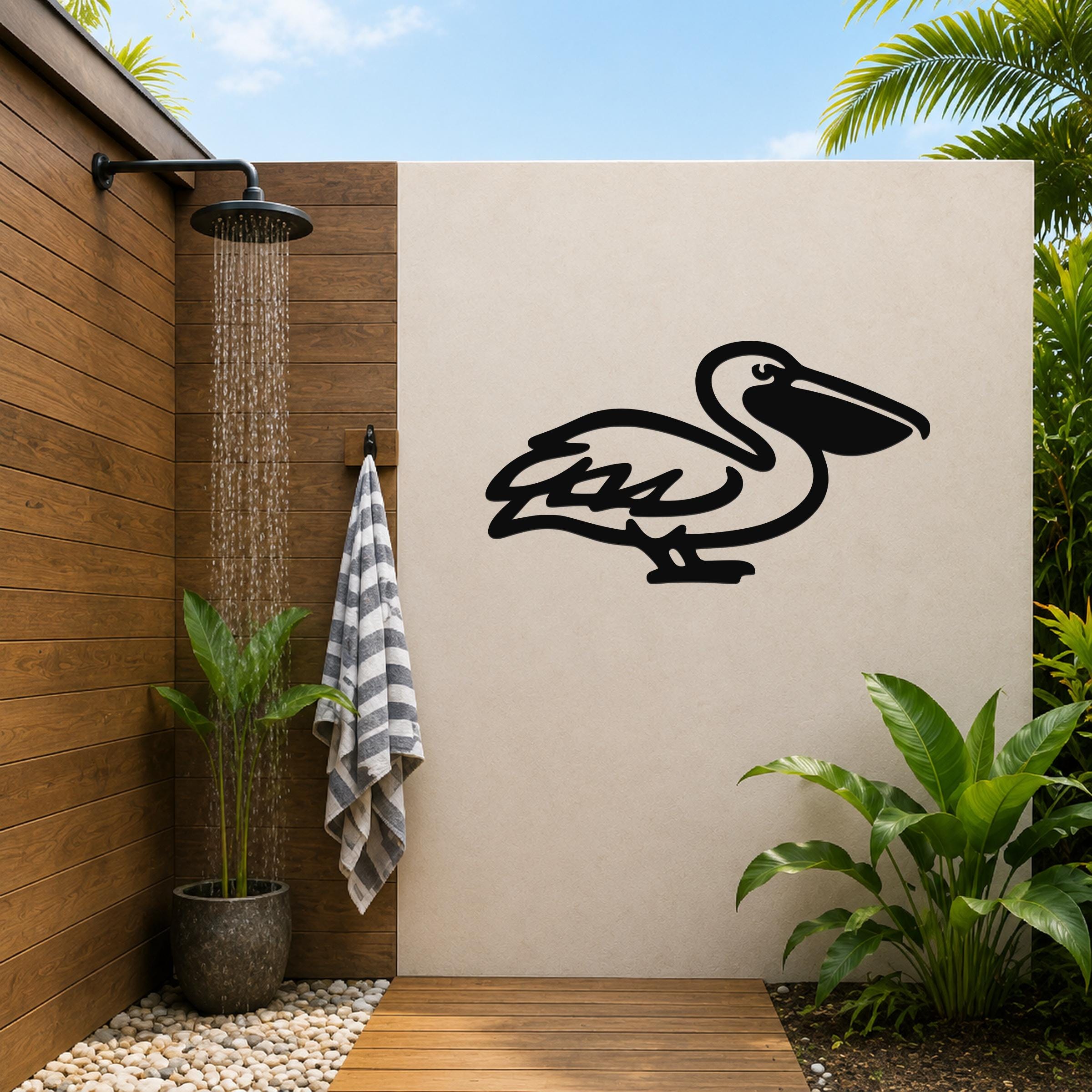 Black metal pelican wall art silhouette mounted on a beige outdoor wall beside a wooden shower area with a running showerhead and tropical plants.