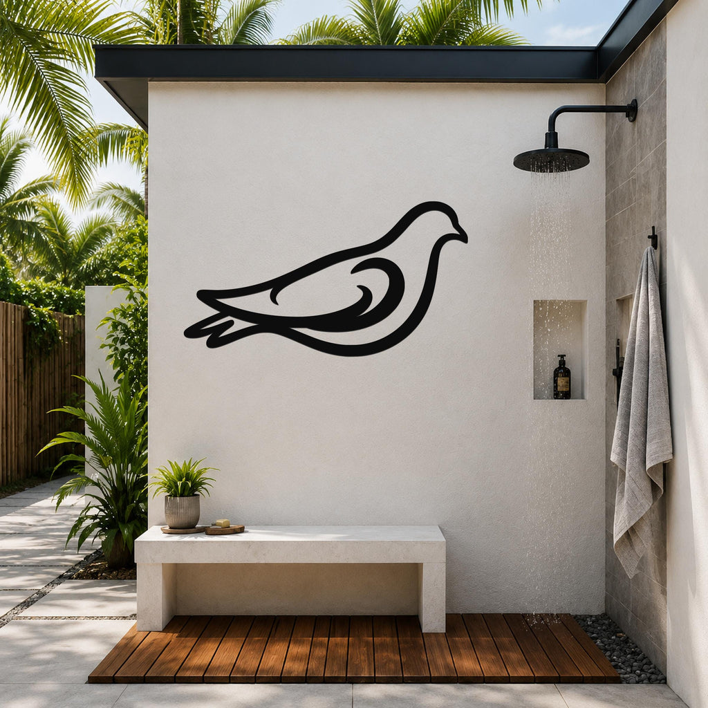 Black metal pigeon wall art silhouette mounted on a white outdoor shower wall, above a concrete bench in a tropical patio setting.