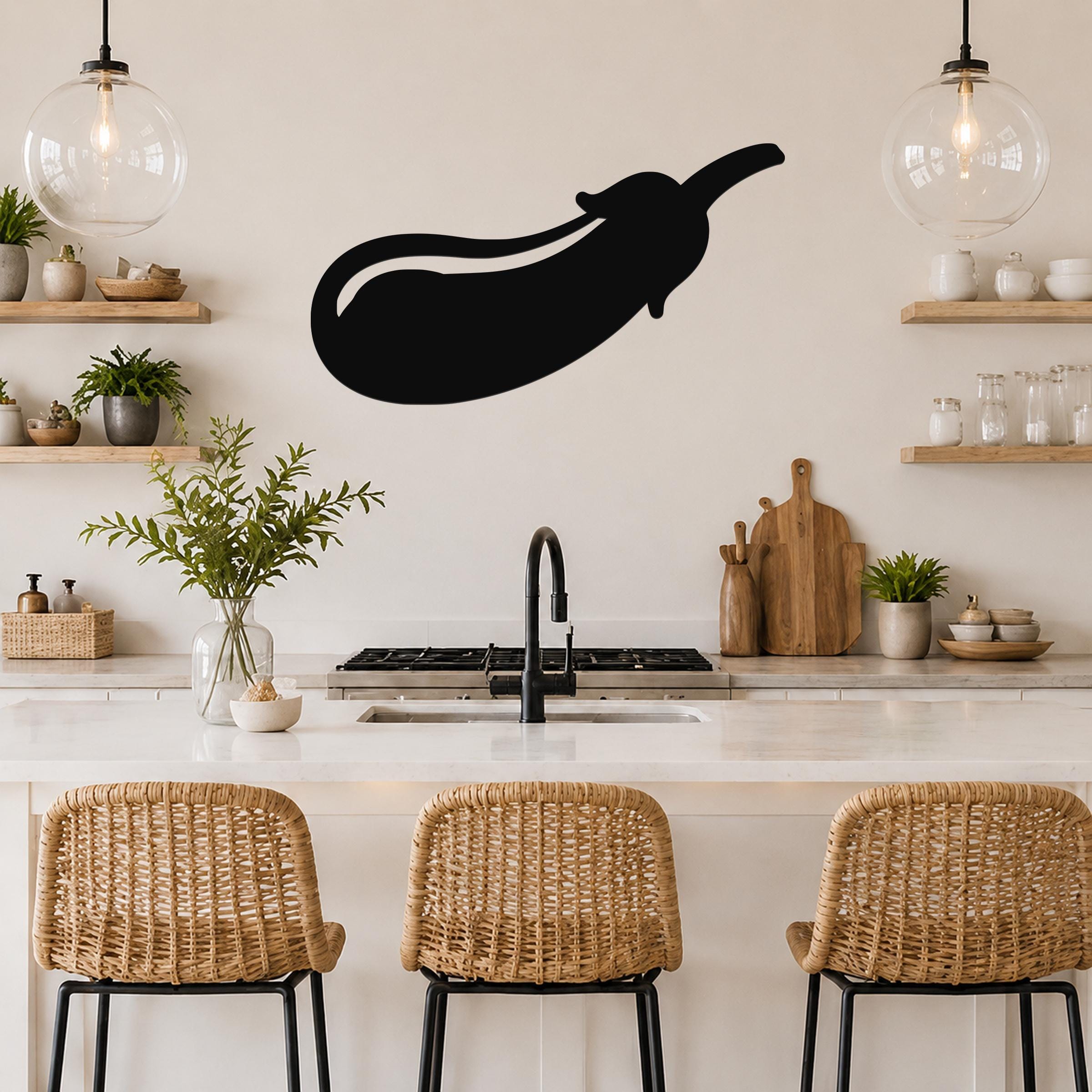 Black metal eggplant wall art silhouette mounted on a kitchen wall above a counter, with a white countertop and woven bar stools below.