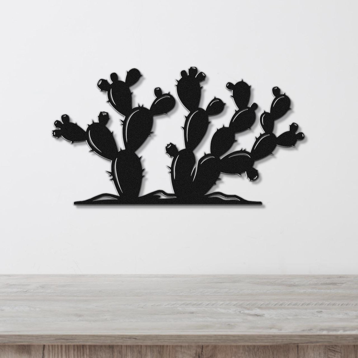 Black metal wall art cutout of a prickly pear cactus with multiple pads and spines, mounted on a white wall above a light wood countertop.