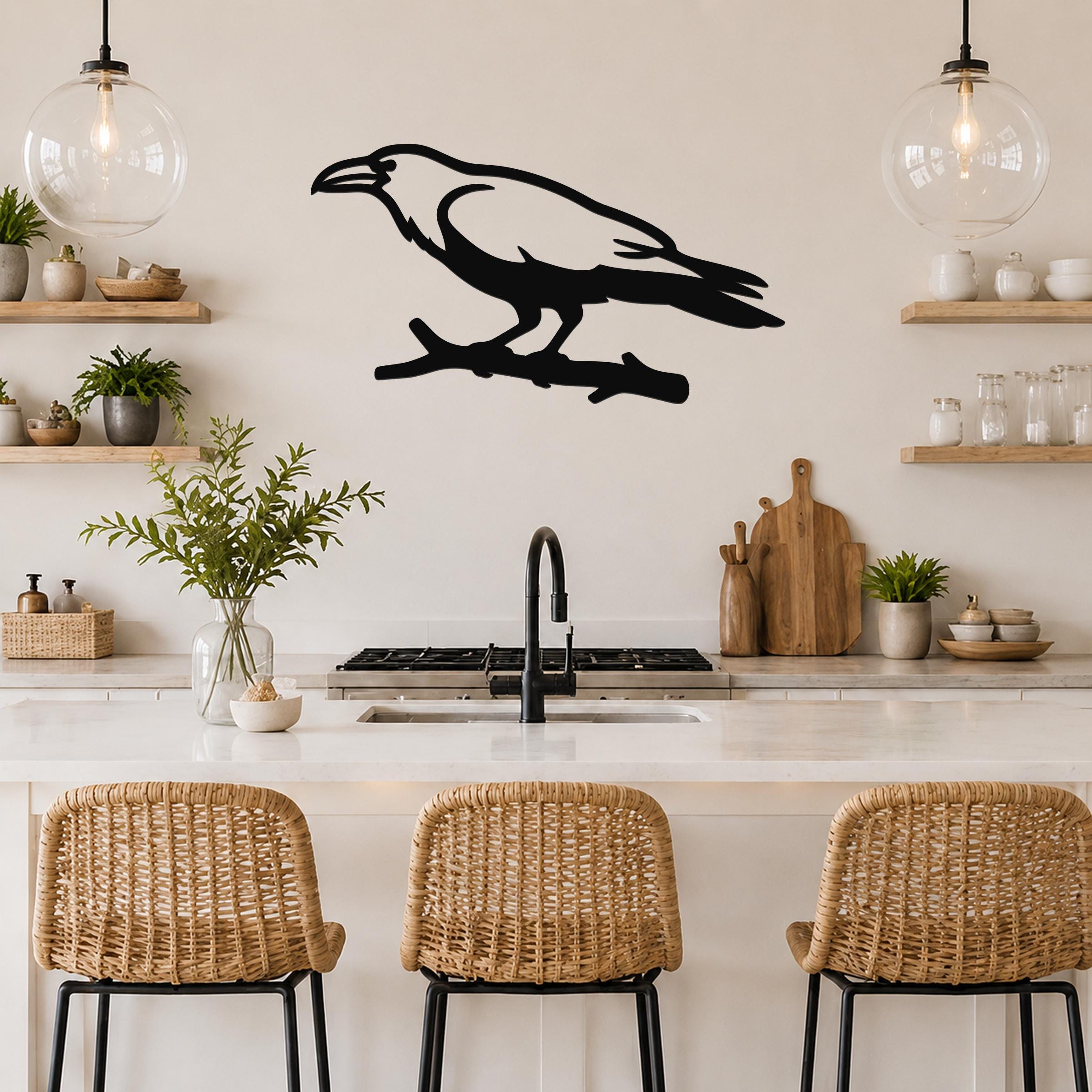 Black metal raven wall art silhouette perched on a branch, mounted above a kitchen counter with open shelving and pendant lights.