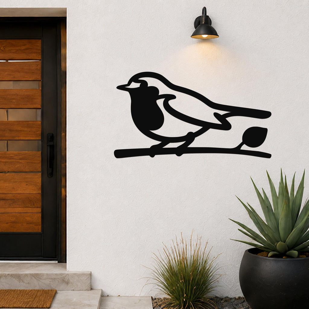 Black metal robin wall art silhouette perched on a branch, mounted on an outdoor wall beside a front door and potted plants.