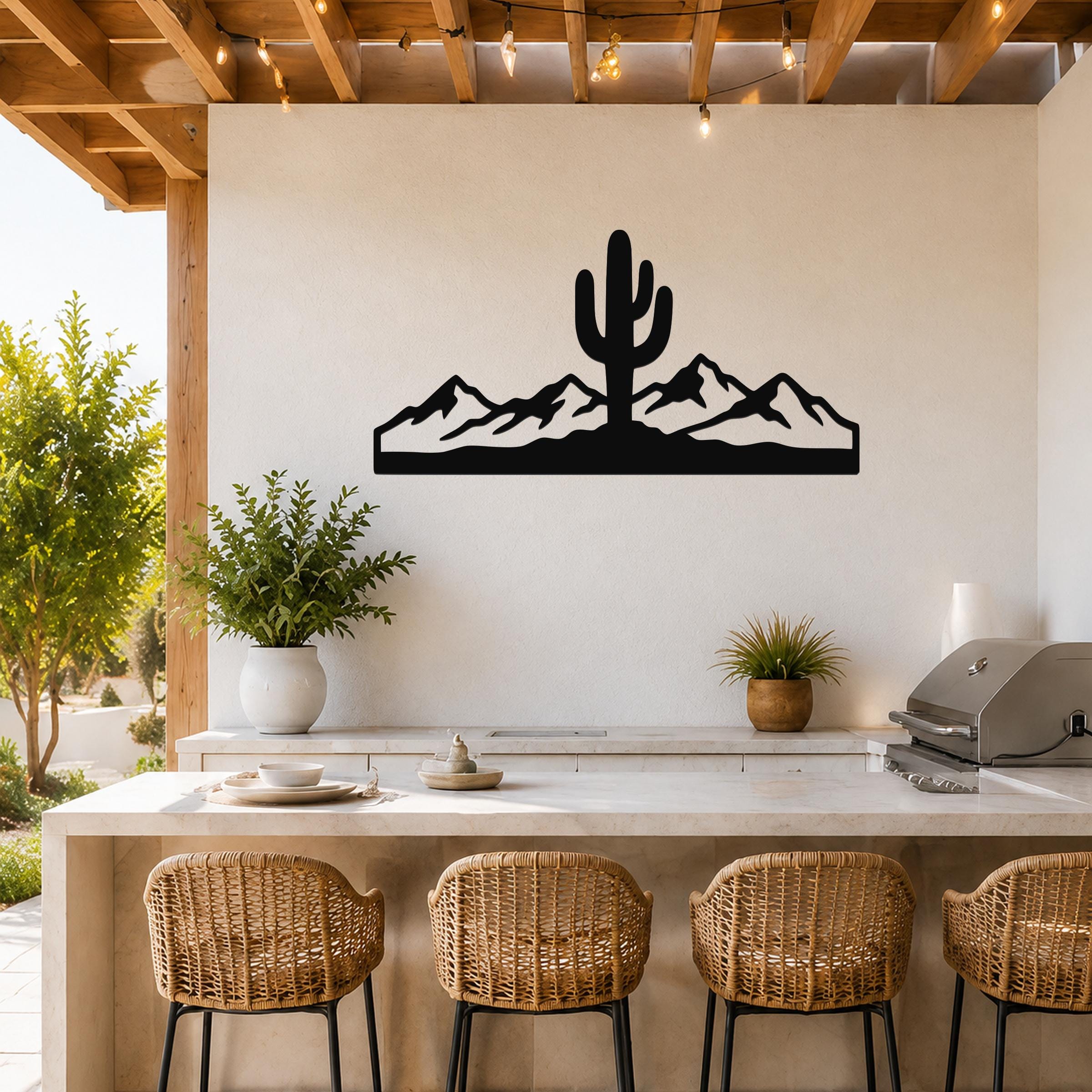 Black metal wall art featuring a saguaro cactus and mountain silhouette, mounted on a white wall above a kitchen counter in an outdoor patio setting.