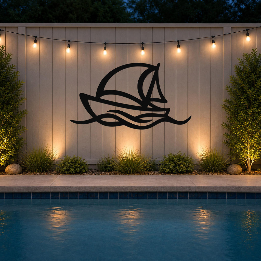 Black metal sailboat wall art with wave cutouts, mounted on a light-colored outdoor wall above a pool at night.