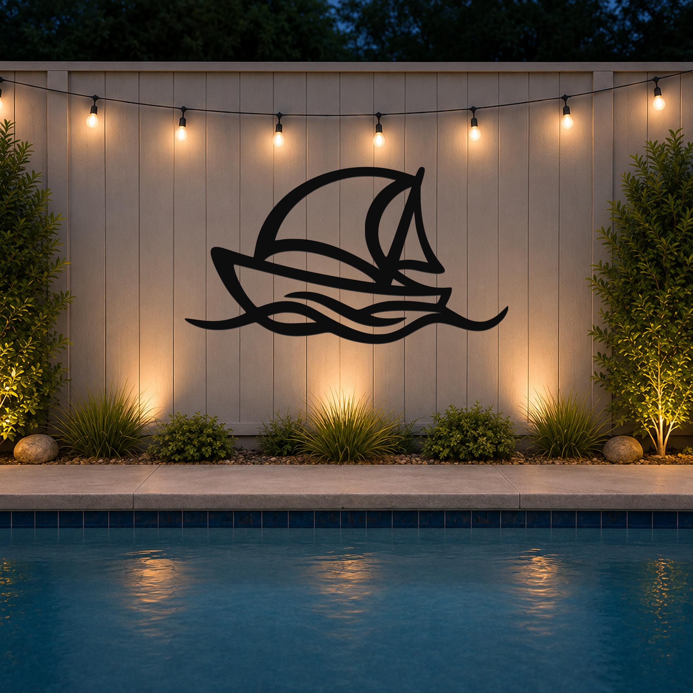 Black metal sailboat wall art with wave cutouts, mounted on a light-colored outdoor wall above a pool at night.