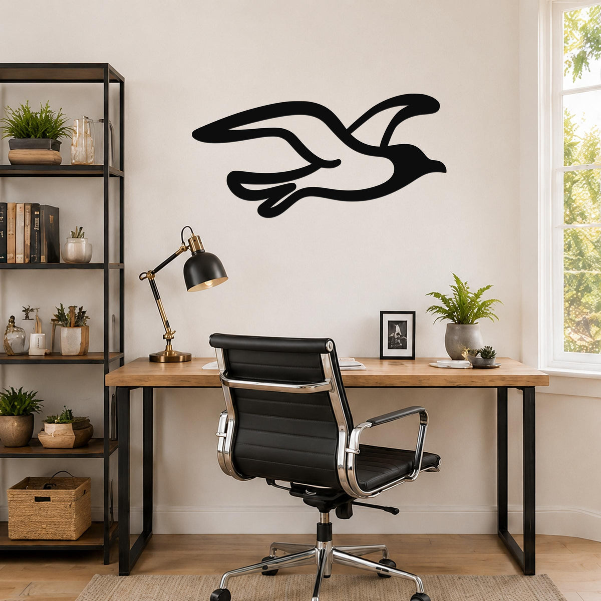 Black metal seagull wall art with flowing wing cutouts, mounted above a wooden desk in a home office.