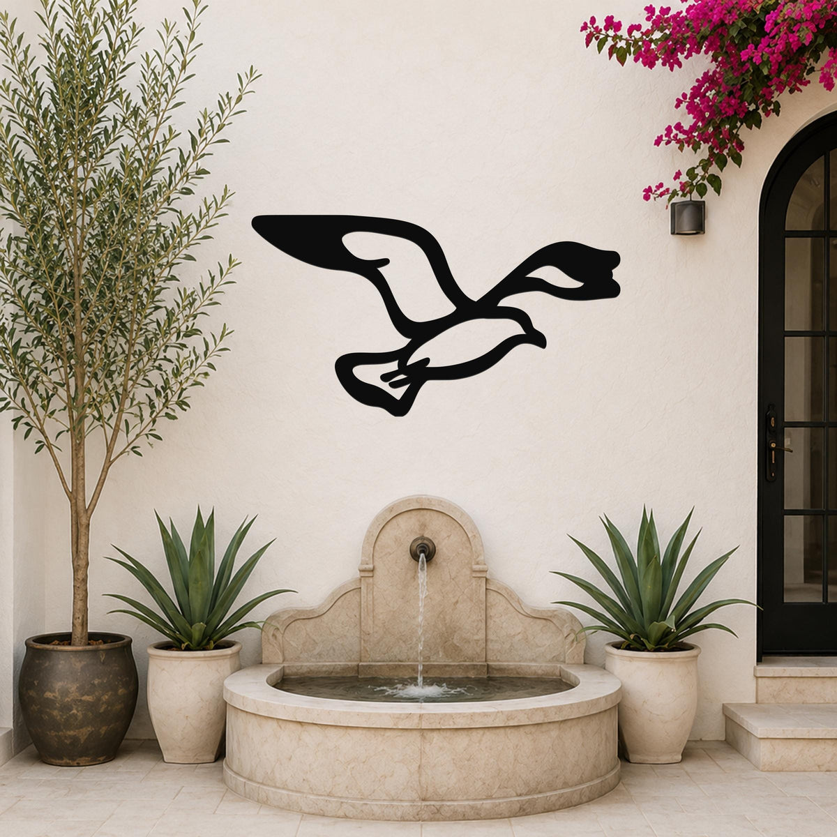 Black metal seagull wall art with wing and tail cutouts, mounted on a white outdoor wall above a stone fountain.